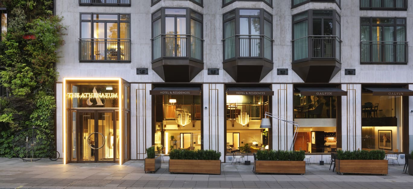 A elegant hotel facade with green awnings and a doorman welcoming a family with children.