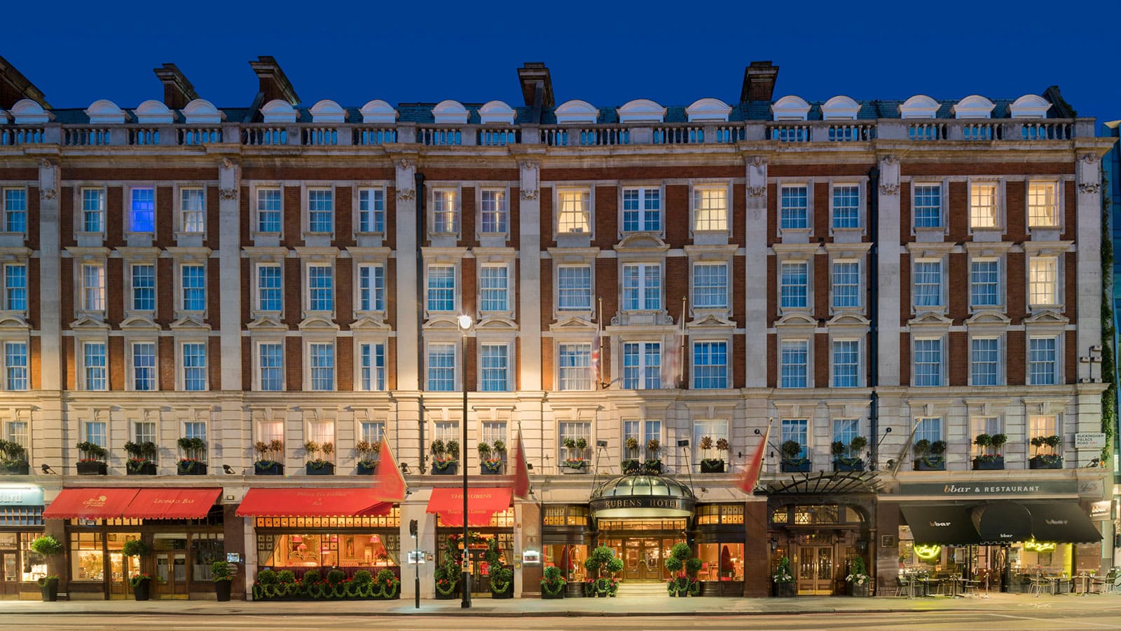 A grand hotel lobby with red carpets and chandeliers, with a family being greeted by staff in traditional uniforms.