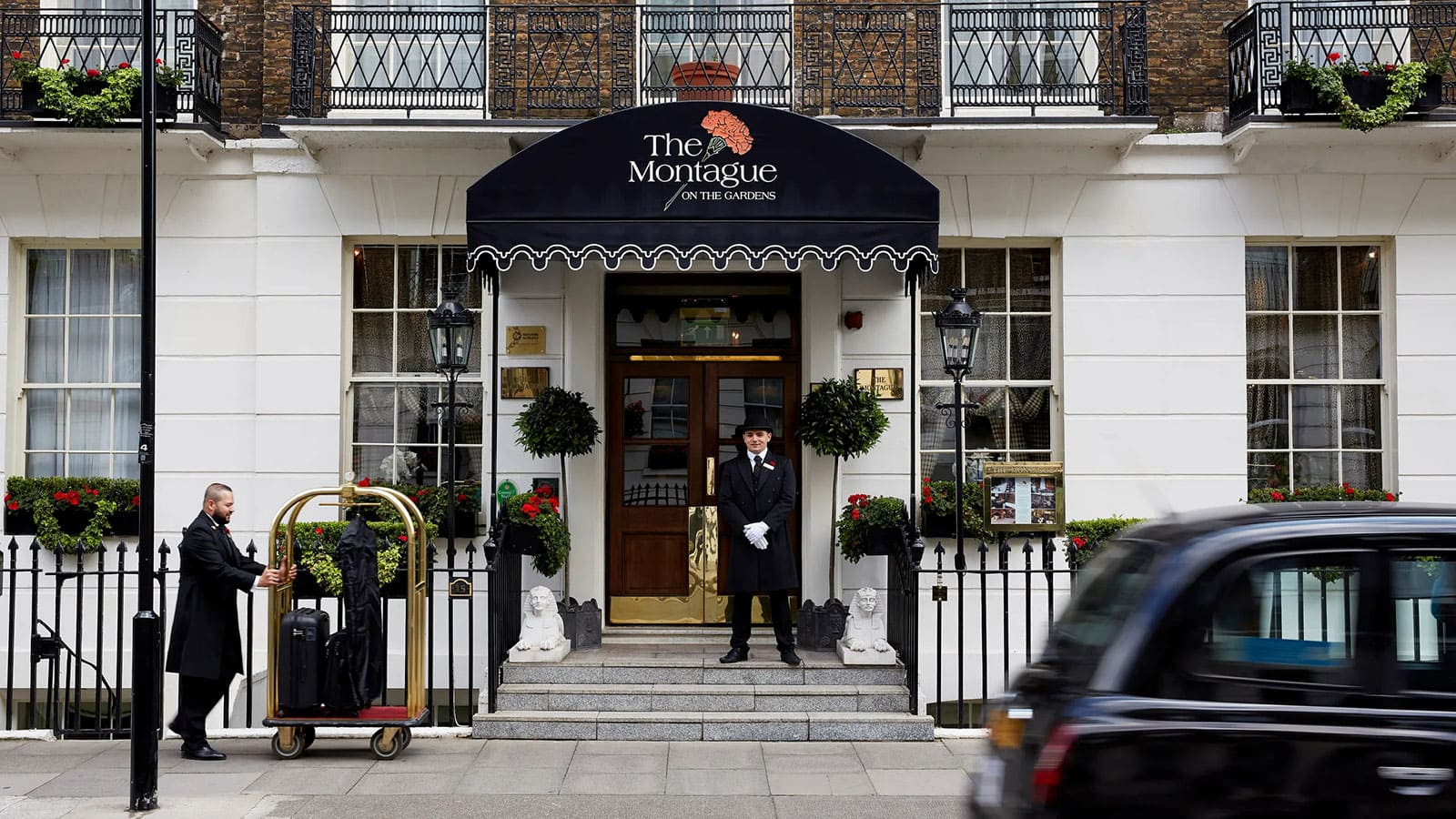 A quaint hotel exterior with flower boxes and a red carpet leading to the entrance.