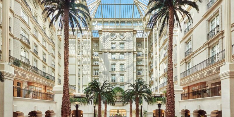 A stunning atrium with palm trees and a glass roof, featuring families enjoying afternoon tea.